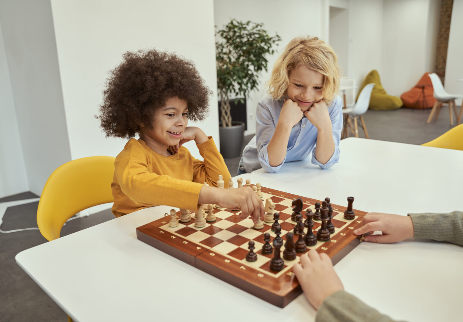 Cheerful little diverse boys sitting at the table and playing chess in school. Mind sport and board games, education concept